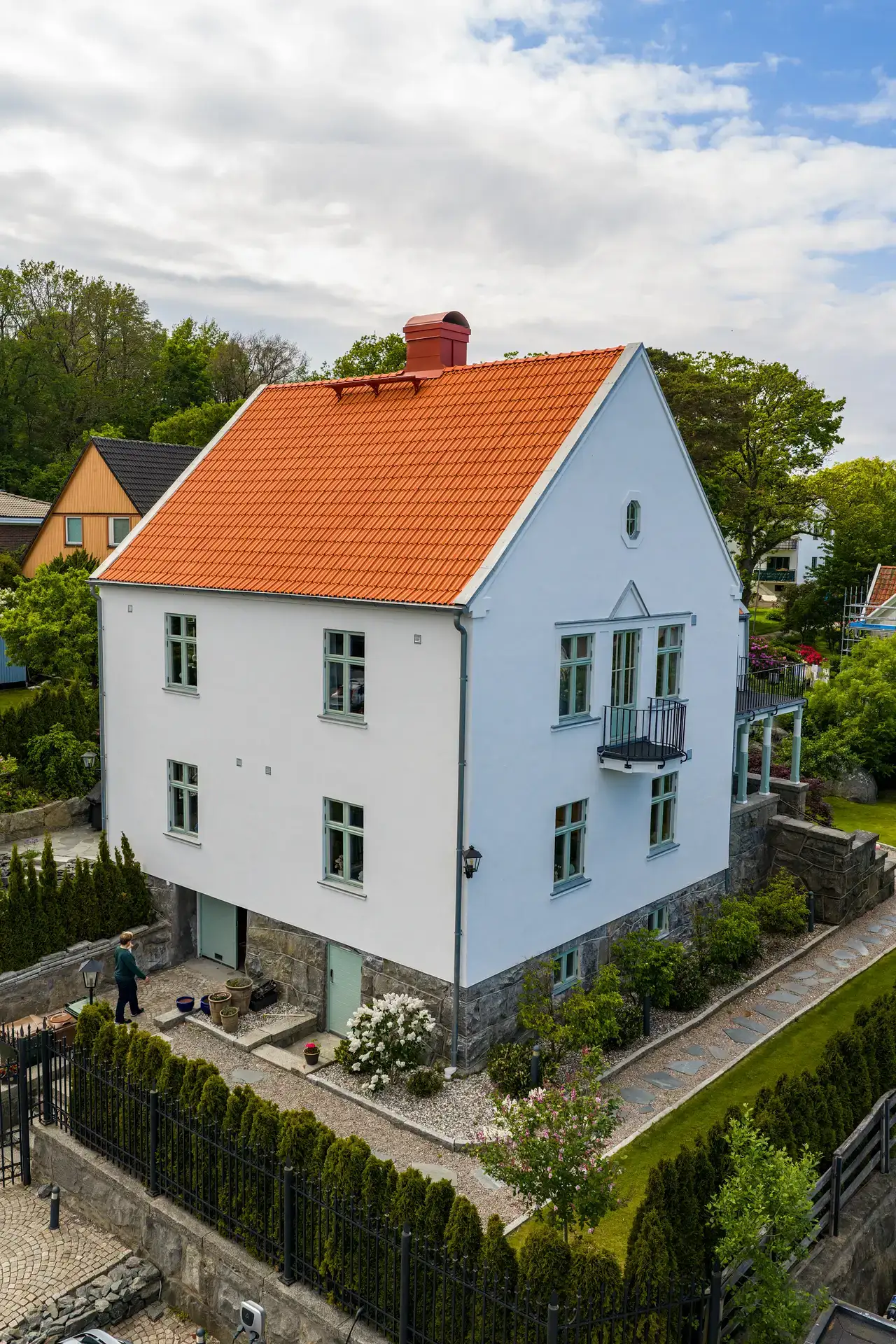 Vit tvåvåningsvilla med orange tegeltак och lummig trädgård.