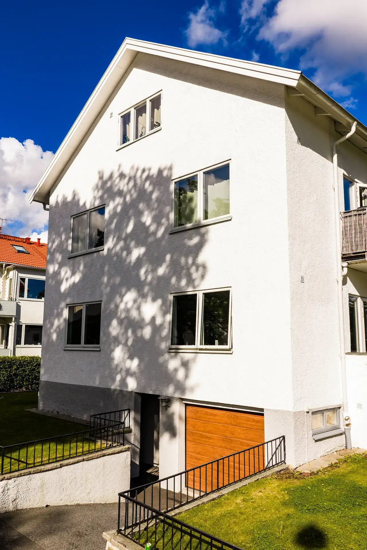 Vit tvåvåningsvilla med garage och svarta räcken under blå himmel.