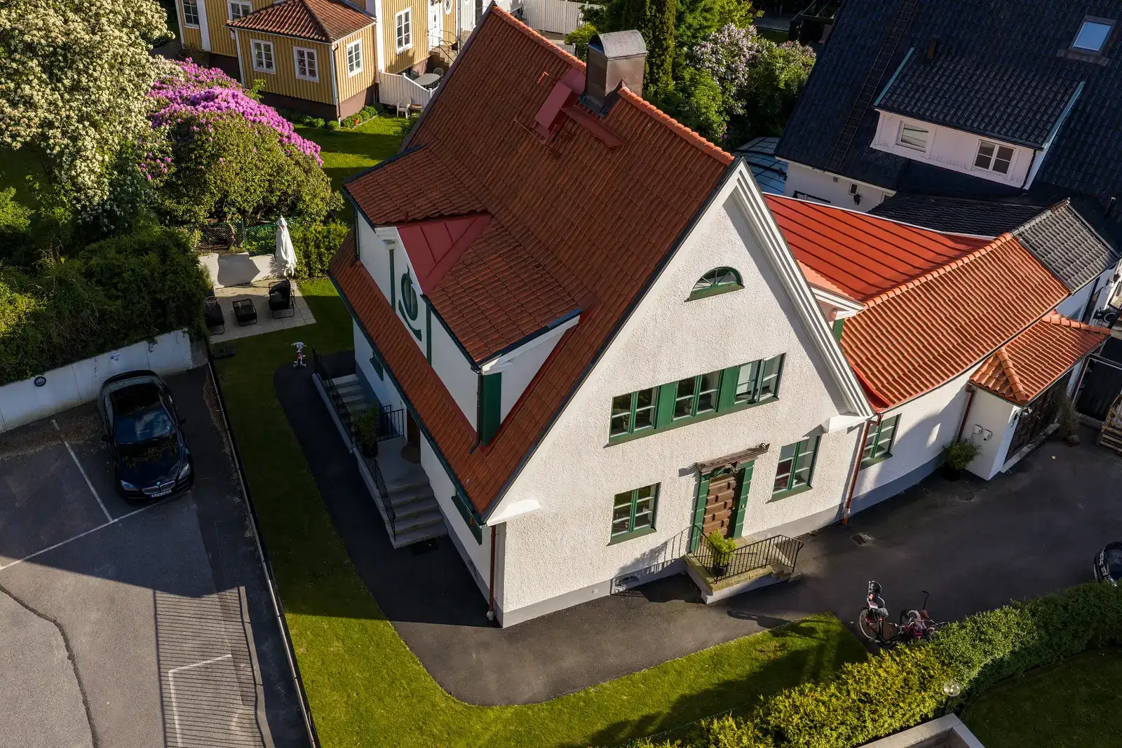 Flygfoto över vit villa med rött tegelttak och gröna fönsterluckor.