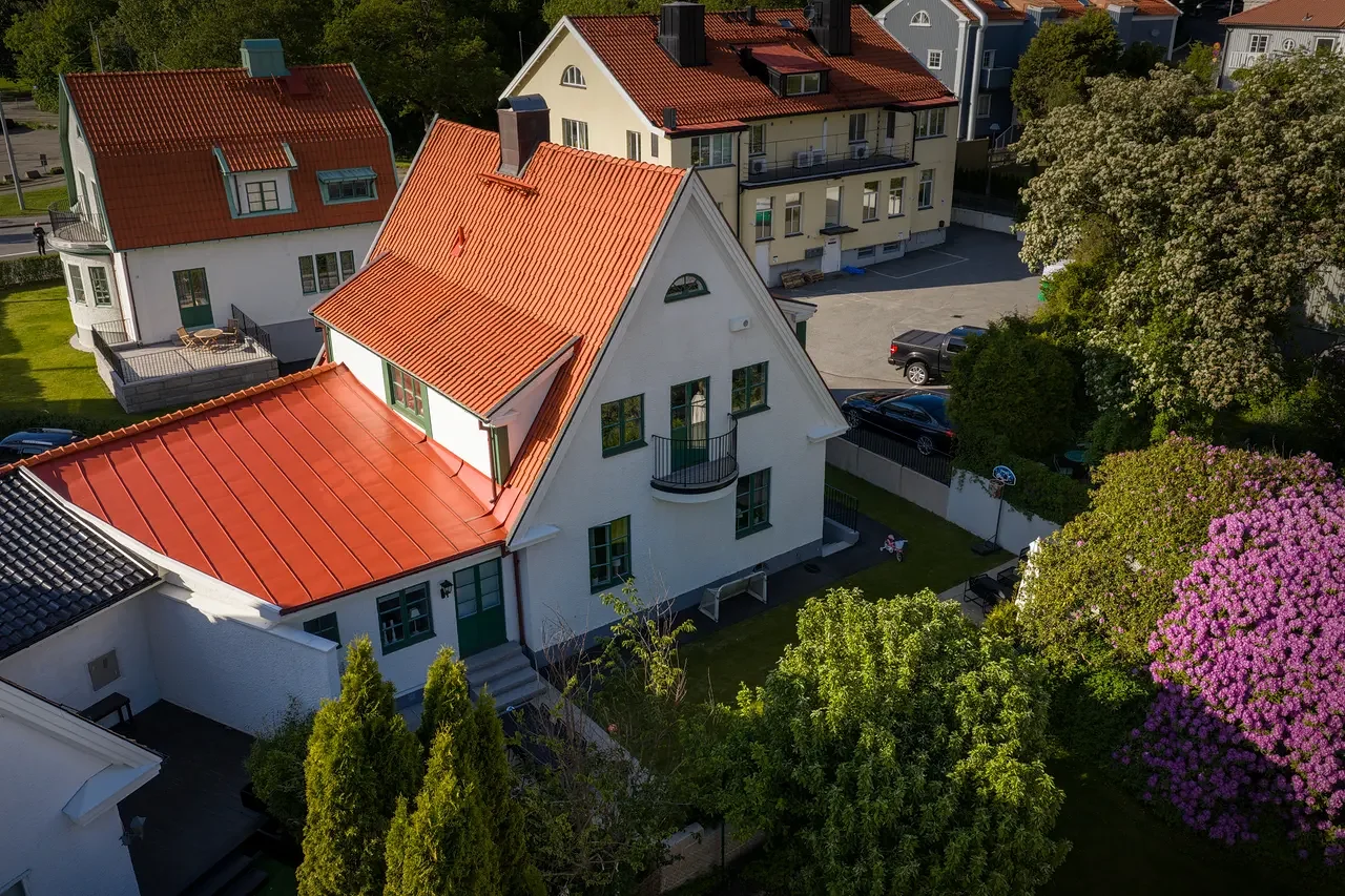 Flygfoto över vita villor med röda tegeltak omgivna av grönska.