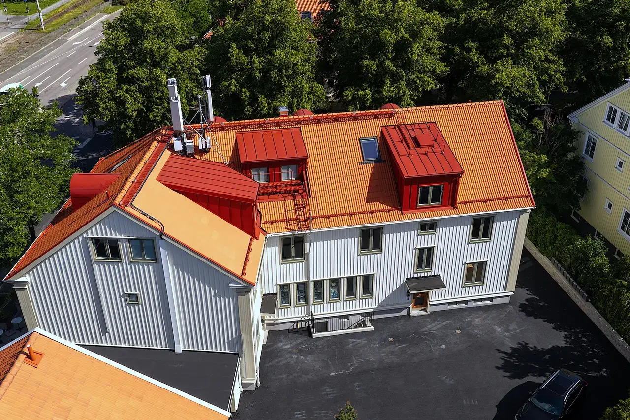 Flygfoto över vit byggnad med orange tegeltак och röda takkupor.