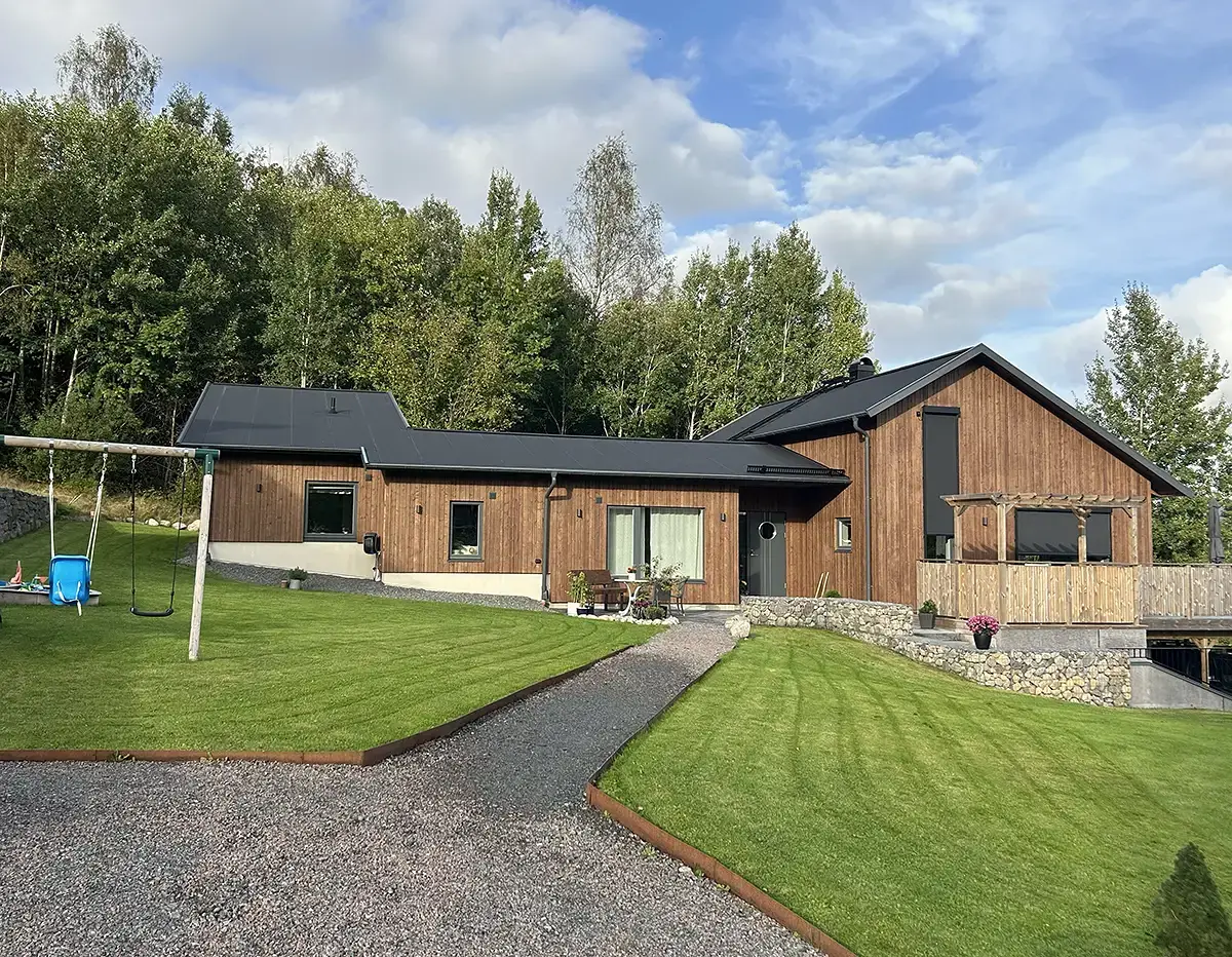 Modernt trähus under konstruktion med naturlandskap och byggmaterial framför.