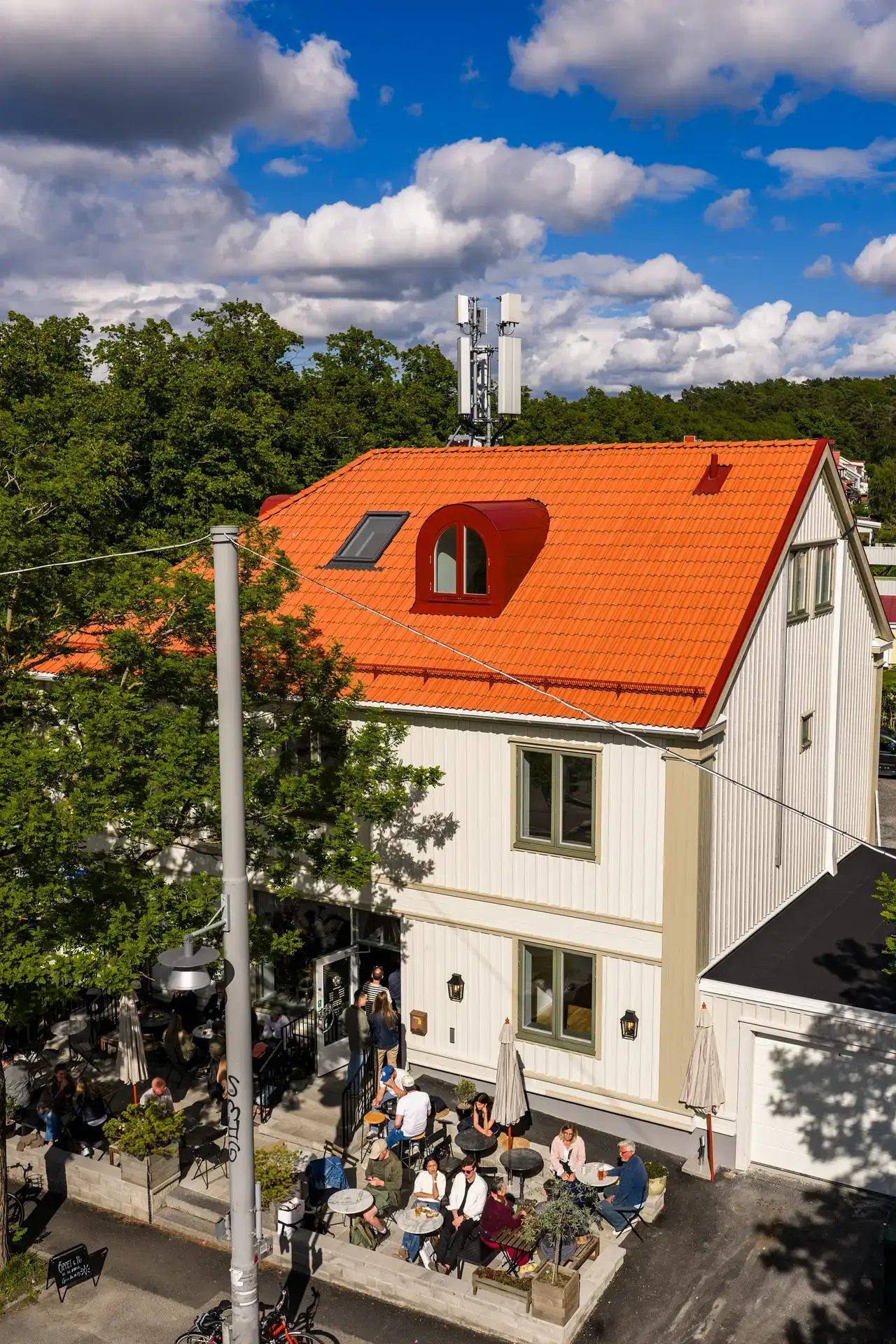 Uteservering vid vitt hus med orange tegeltак en sommardag.