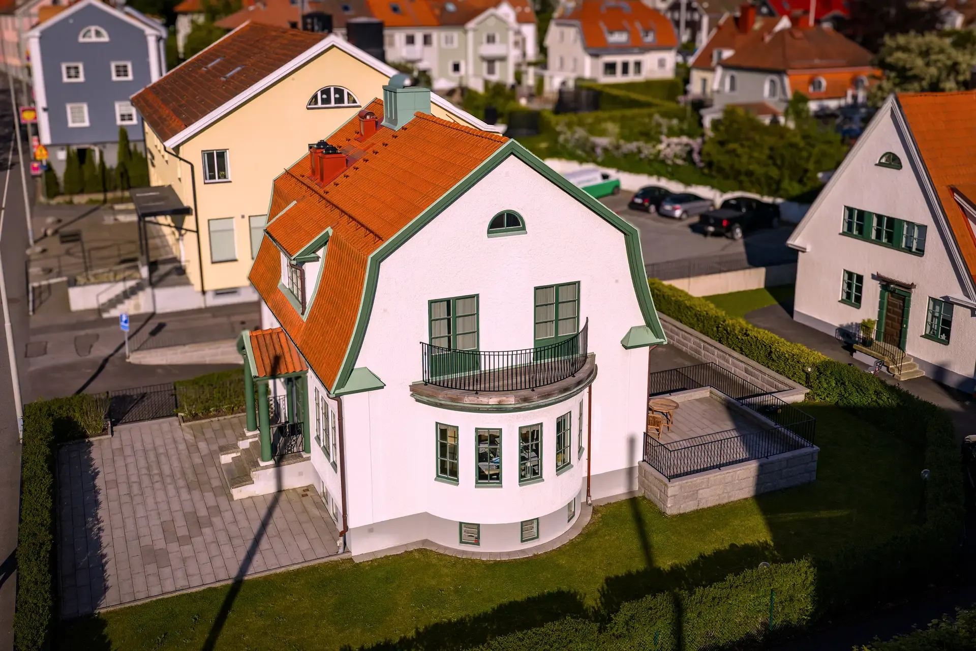 Flygfoto över vit villa med orange tegeltak och grön balkong.